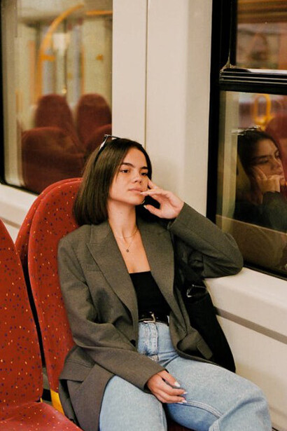 A Gen Z girl in a blazer and vintage sunglasses, reflecting a mix of past and present style on the train