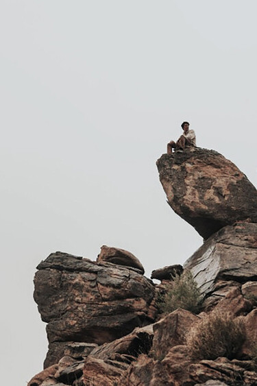 A man in a black jacket sits on a rock formation in broad daylight