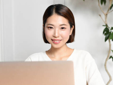 A young Asian woman smiling as she looks at her laptop