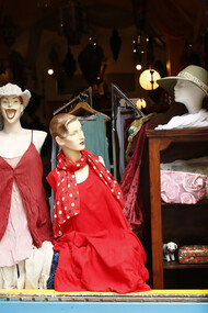 A pair of mannequins displayed in a shop window, showcasing quirky styles in a charity shop that promotes second-hand shopping and sustainable fashion