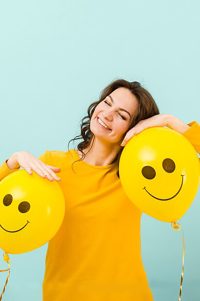 A woman smiling as she holds balloons with cheerful faces, captured from the front, radiating happiness