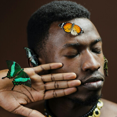 Un retrato sereno y poético de un hombre con el torso desnudo inmerso en la naturaleza, donde las mariposas revolotean a su alrededor como símbolos de transformación y armonía.