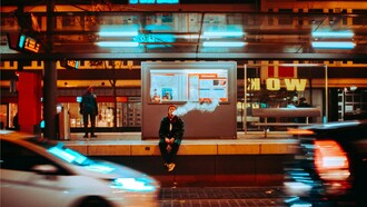 A man sitting at a bus stop and vaping, reflecting how people often turn to vaping as a way to cope with stress or anxiety in an increasingly hectic world