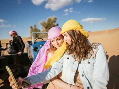 Two women stand beside a blue Land Rover during a desert safari in the United Arab Emirates