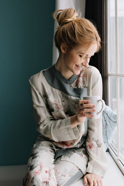Sitting by a big window, a young blonde woman enjoys her tea, embracing the tranquility of her peaceful home environment