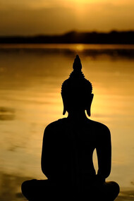 A Buddha statue seated peacefully in front of a calm body of water