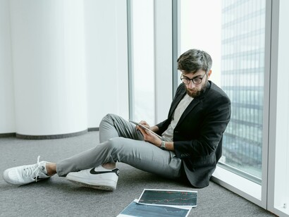 A young worker seated on the floor, looks at his tablet with quiet frustration