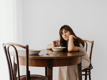 A woman leaning on a table, an empty chair bearing silent grief