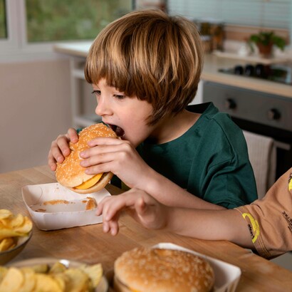 Bambino che mangia un hamburger a casa: "una dieta povera di fibre e ricca di cibi processati può causare patologie metaboliche e resistenza all’insulina"