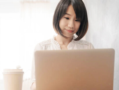 A young Asian woman looking at her laptop screen with a cheerful expression