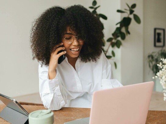 A Gen Z woman sits in front of her laptop and tablet, multitasking between work and digital tasks, and speaking on the phone