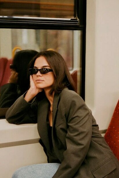 A Gen Z girl on a train, wearing a blazer and vintage sunglasses, blending nostalgia with modern style