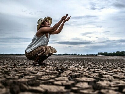 A man sitting on dry, cracked ground, representing the harsh realities of water scarcity in a resource-stressed world