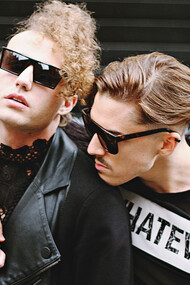 Dois homens abraçados com visual inspirado na moda punk e gótica. A Versace Spring–Summer 2023 trouxe elementos dramáticos e góticos, fazendo referências sacras com véus, crucifixos e muitas texturas