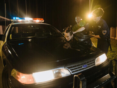 Police officer arresting a suspect by guiding a man in a black jacket against a police car