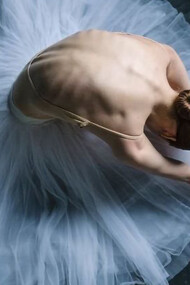 A ballet dancer gracefully leans towards the floor, her focus on her feet and form