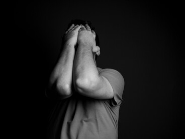 Grayscale photo of a man covering his face with his hands, expressing intense anxiety or emotional distress