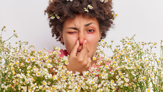 A woman with breathing difficulties holds her nose, suffering from allergies; she clutches a large bouquet of flowers and has red, itchy eyes
