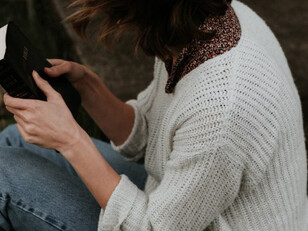 A woman sits on the gray concrete pavement, deeply engrossed in reading her Bible, finding peace in the quiet moment