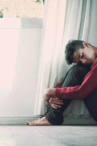 A barefoot young man hugging his legs, trying to sooth himself