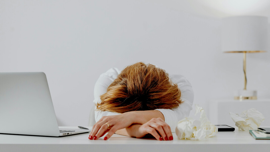 A female writer resting her head on the table beside a laptop, looking anxious and depressed