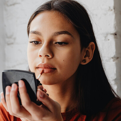 A woman puts on lipstick in front of a mirror, completing her makeup look