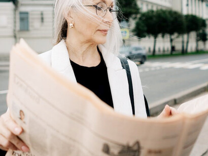 A senior woman on the street, absorbed in her newspaper, capturing a moment of French media life