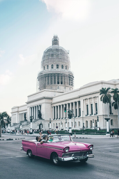 An old pink convertible coupe parked in front of the El Capitolio building in Havana, Cuba