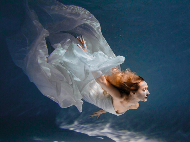 A graceful body suspended in water in a flowy white dress, conveying a weightless, unhurried state that mirrors emotional release