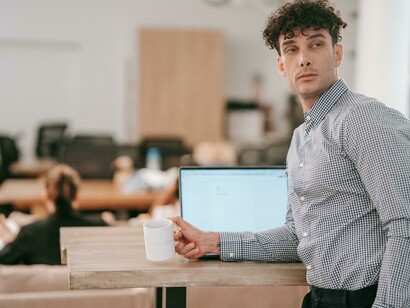 A young man relaxes in a café, sipping coffee as he types on his laptop