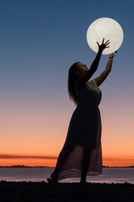 Mulher brinca com projeção com uma lua inflável no atardecer na praia