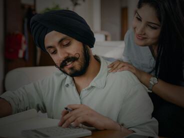 An Indian couple using a calculator and taking notes while budgeting their monthly living costs