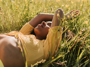 Woman in yellow lying on grass, getting sunlight for vitamin D