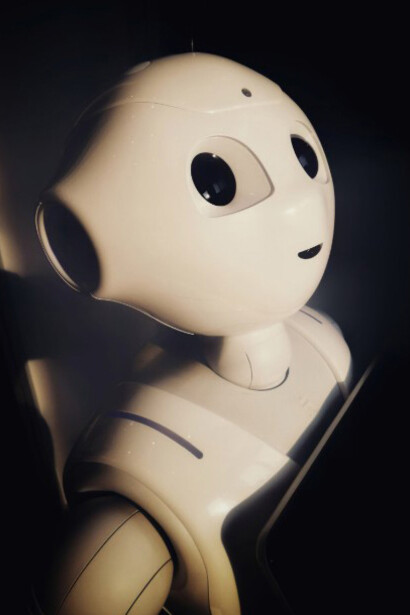 A white robot toy holding a black tablet, representing AI companions, virtual friends, and robotic therapy