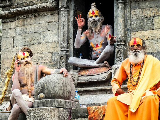 Three monks resting on the concrete steps of Pashupatinath Temple during the daytime, embodying the serene spirituality of Kathmandu, Nepal