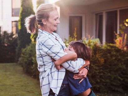Una donna e il suo bambino sorridono, alle loro spalle si vede la loro casa