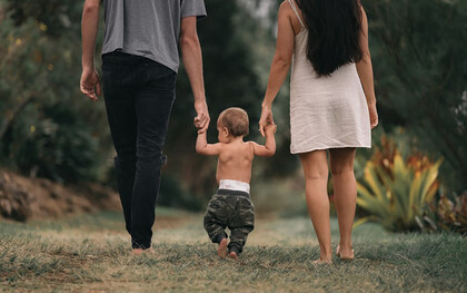 A couple walks barefoot through the garden, holding hands with their child