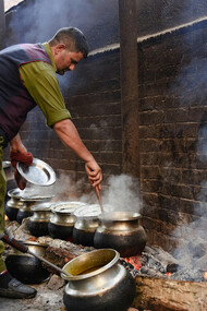 A man stirs food in large pots over an open flame, preparing a traditional meal, Srinagar, India