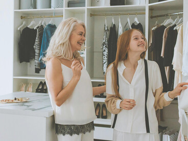 A grandmother and granddaughter selecting clothes from a wardrobe bathed in soft natural light, embodying quiet luxury and the elegance of timeless, neutral-toned fashion