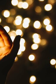 A hand holding a small light against a backdrop of little lights, weaker than a single illuminating focus, but plural and decentralized