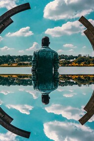 A man's self reflection, framed by a sculpture and the sky