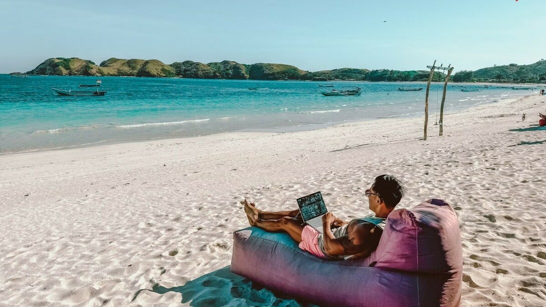 A man sitting on a bean bag on the beach, working on his laptop in Lombok
