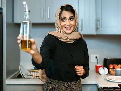A health-conscious woman, clutching a bottle of olive oil, is poised to embark on a nutritious cooking endeavor