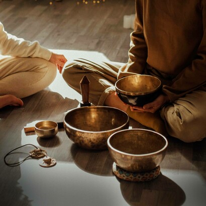 Due persone sedute a gambe incrociate, circondate da campane tibetane e altri strumenti per la meditazione sonora