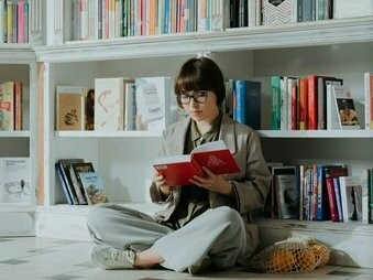 Mulher escolhe livro em estante. Certos dias preferimos o refúgio na natureza, enquanto em outros sentimos necessidade de acelerar o ritmo 