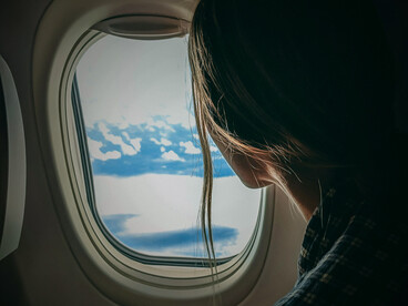 A hand reaches out to the sky through the airplane window, capturing a moment of wonder above the clouds