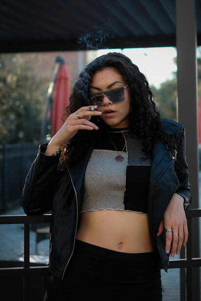 A woman in sunglasses, exuding style, enjoys a smoke outside