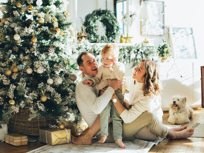 A happy family sitting on a rug beside a traditionally decorated Christmas tre