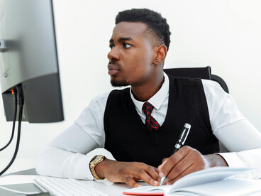 A Black man working at his office desk, appearing tired and stressed