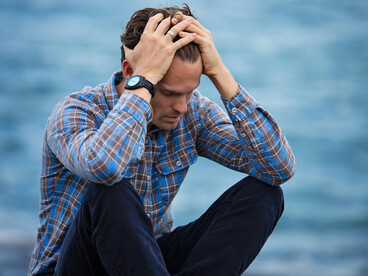 A sad and lonely man in a blue and brown plaid shirt touches his hair in despair
